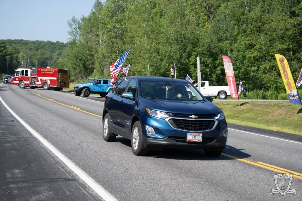 A blue Chevy Equinox flying American flags joins the 2026 procession along the route.