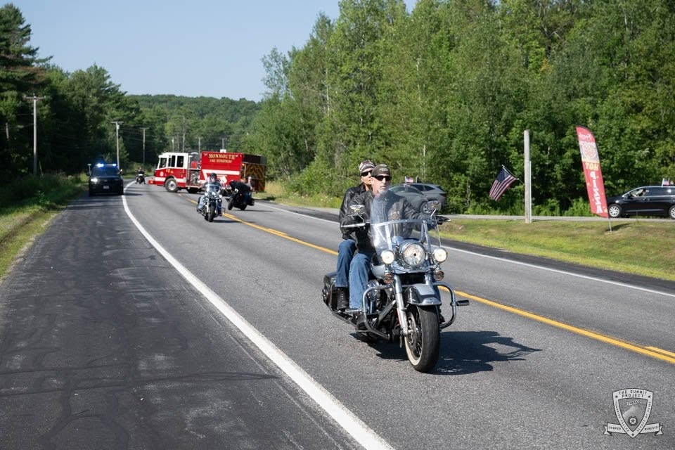 A rider on a classic Harley leads the pack with the fire truck and support vehicles following.