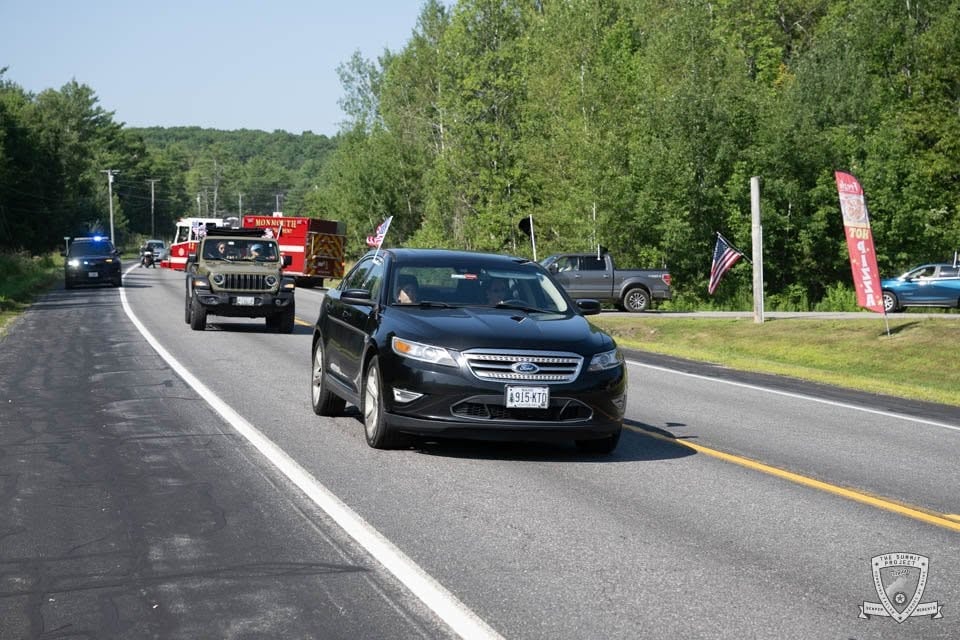 A black Ford Taurus leads a line of vehicles with the olive Jeep and Monmouth FD truck behind.