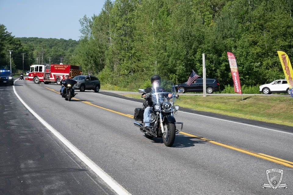 Two riders lead the 2026 procession with a long line of vehicles stretching back down the road.