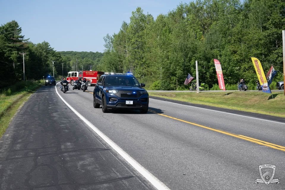 A law enforcement SUV with lights activated leads the 2026 procession out of North Monmouth.