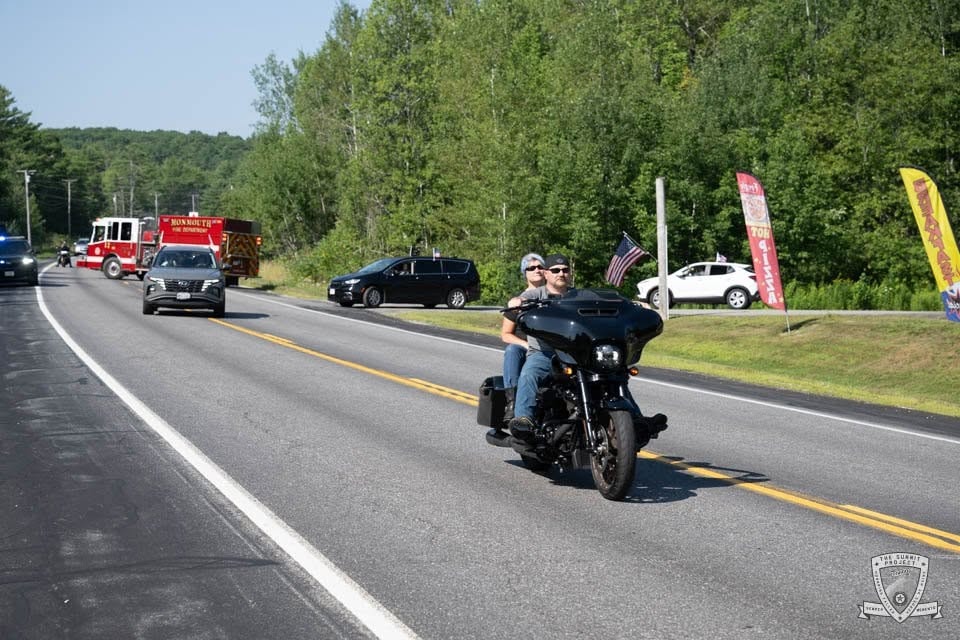 A motorcyclist leads the parade on the highway with the procession stretching behind.